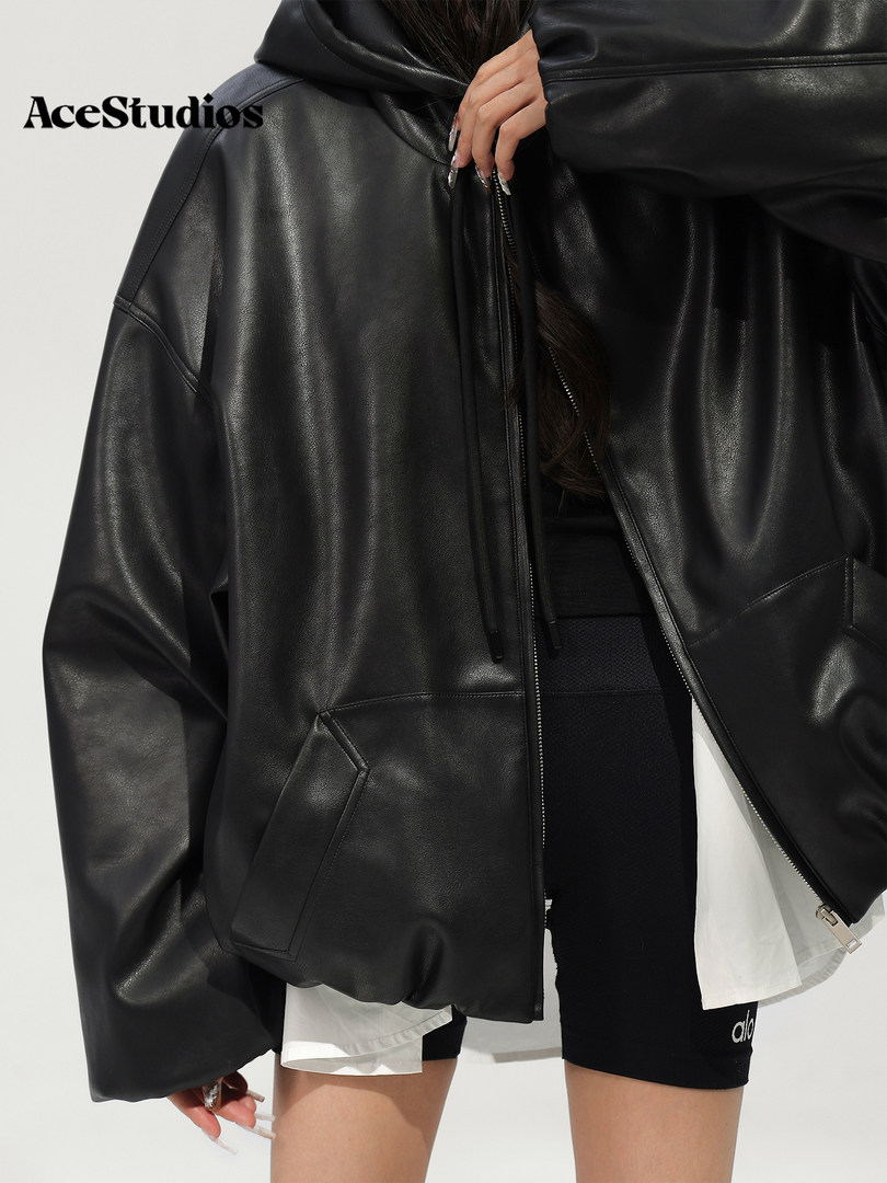 Model wearing a black leather hooded jacket with zip closure and oversized fit