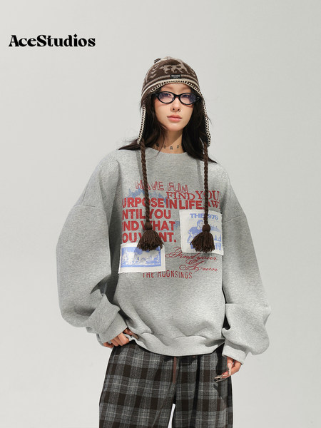 Model wearing a gray graphic sweatshirt, plaid pants, knit earflap hat, and sunglasses.