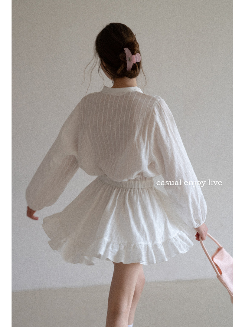 Model wearing a white airy blouse and skirt set with a pink hair clip and bag