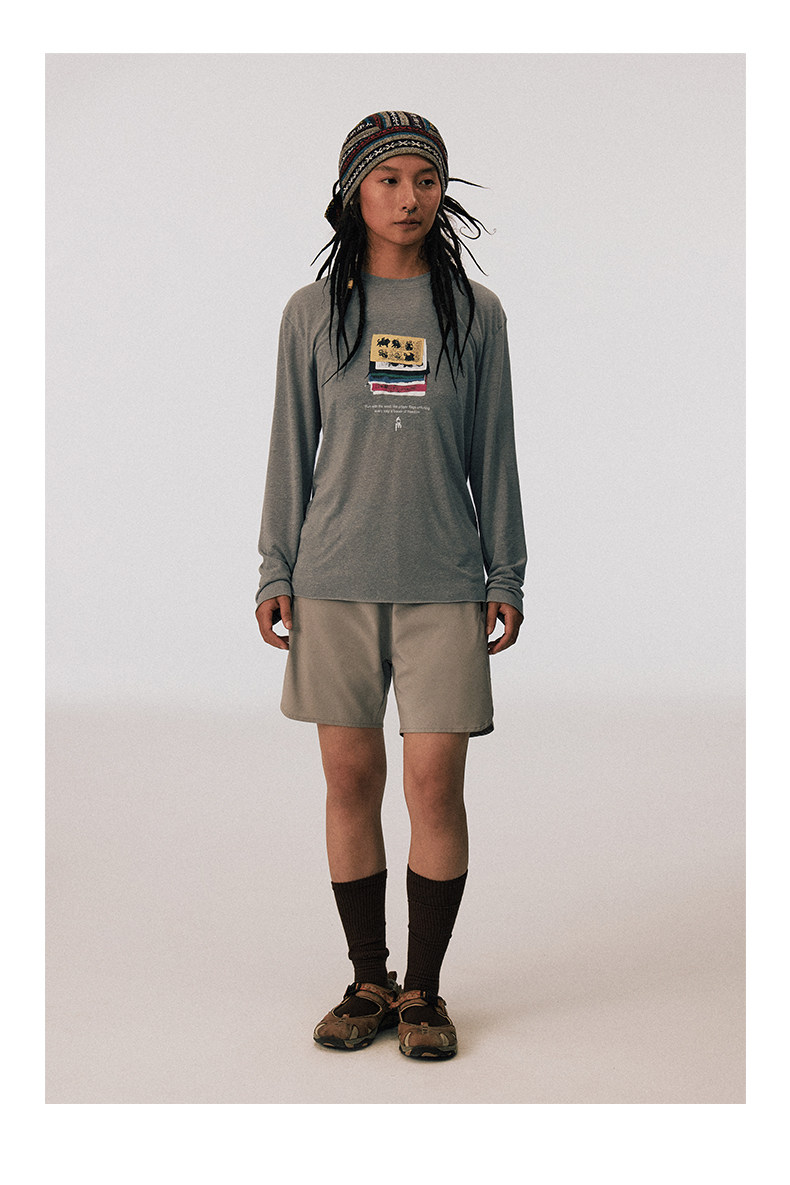 A person faces forward against a plain light background, wearing an EastLyst Vintage vintage T-shirt with a graphic, a patterned headband, beige shorts, dark socks, and brown sandals.