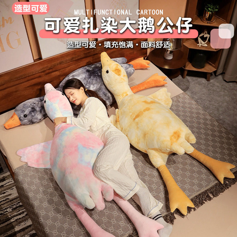 A cute seven-color big goose white doll, plush toy, tie-dyed throw pillow, doll. A girl is sleeping with her legs crossed on the bed