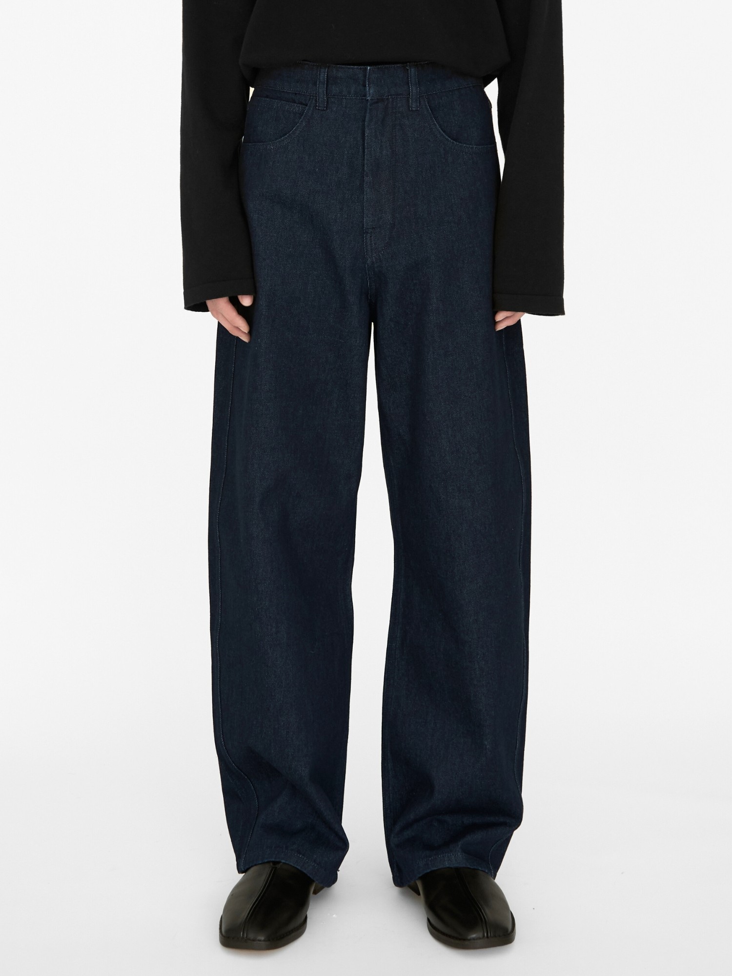 A person wearing EastLyst Turkish Cotton Jeans in dark blue, paired with a long-sleeved black top and black shoes, stands against a plain white background. The photo is cropped from the shoulders down.