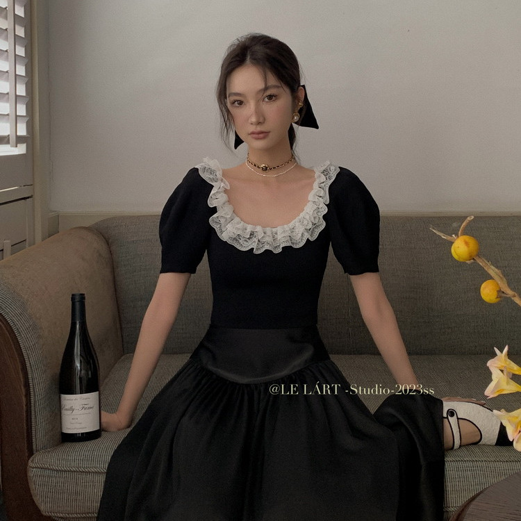 Black puff-sleeve dress with white ruffled lace neckline worn by a model on a sofa