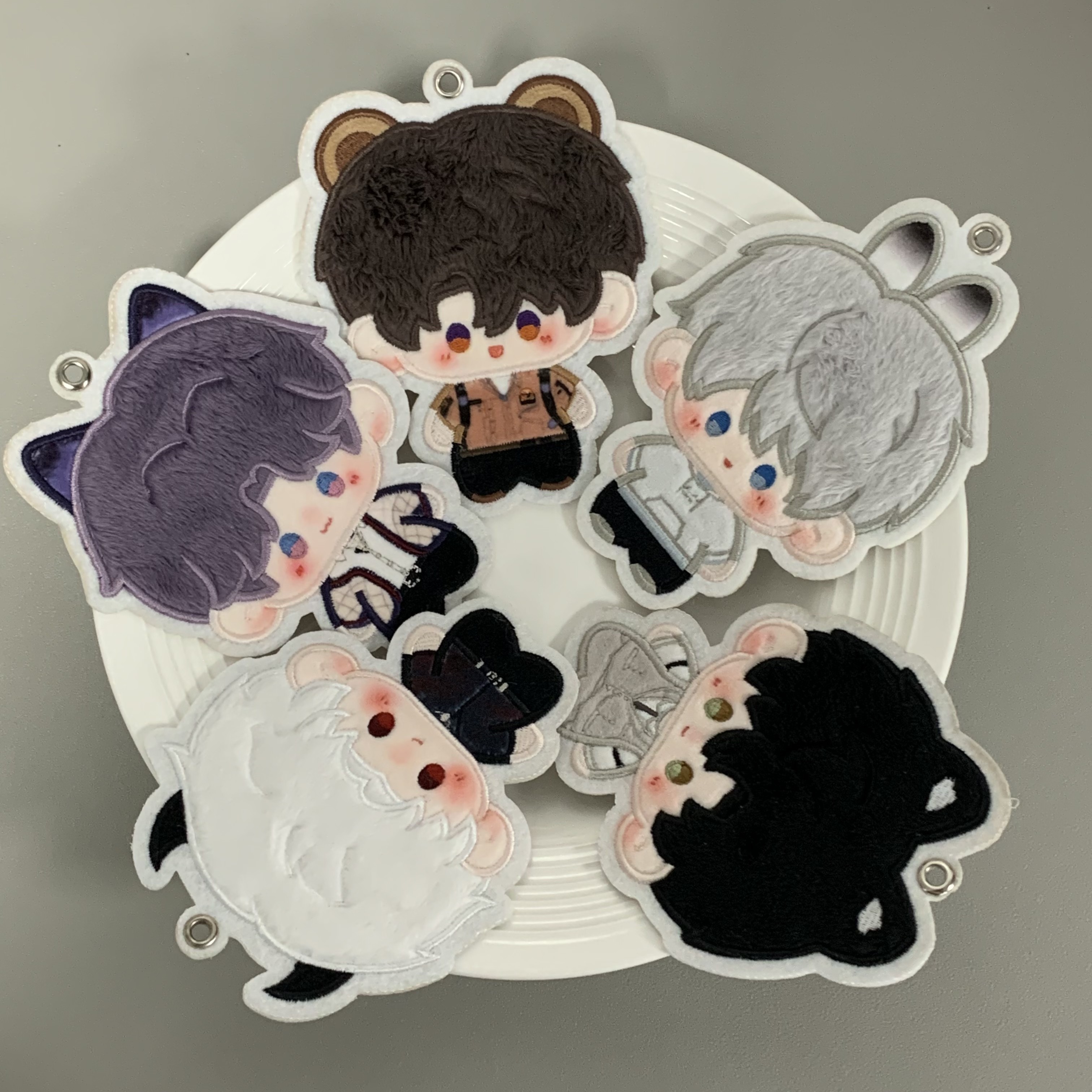 Five embroidered Love and Deepspace character charms on a plate