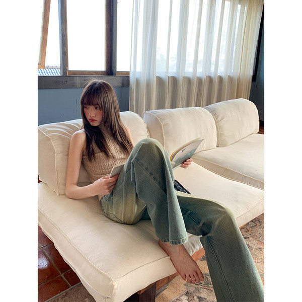 Woman wearing a sleeveless knit top and wide-leg jeans on a sofa