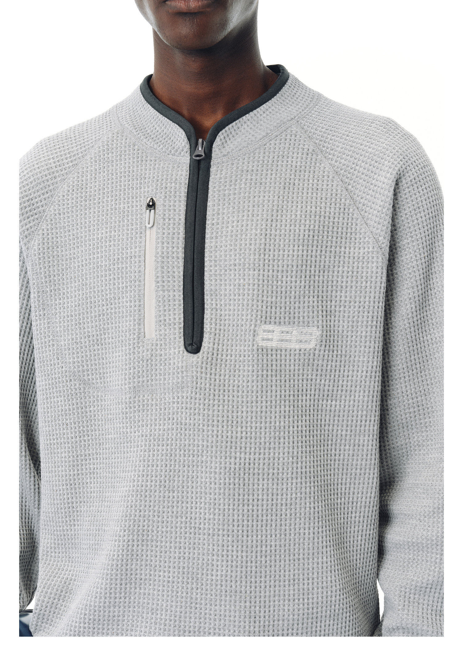 A person wears the EastLyst Heavyweight Magnetic Waffle Knit Pullover Hoodie in light gray, featuring an oversized waffle texture, long sleeves, a short front zipper, and a zippered chest pocket against a white background.