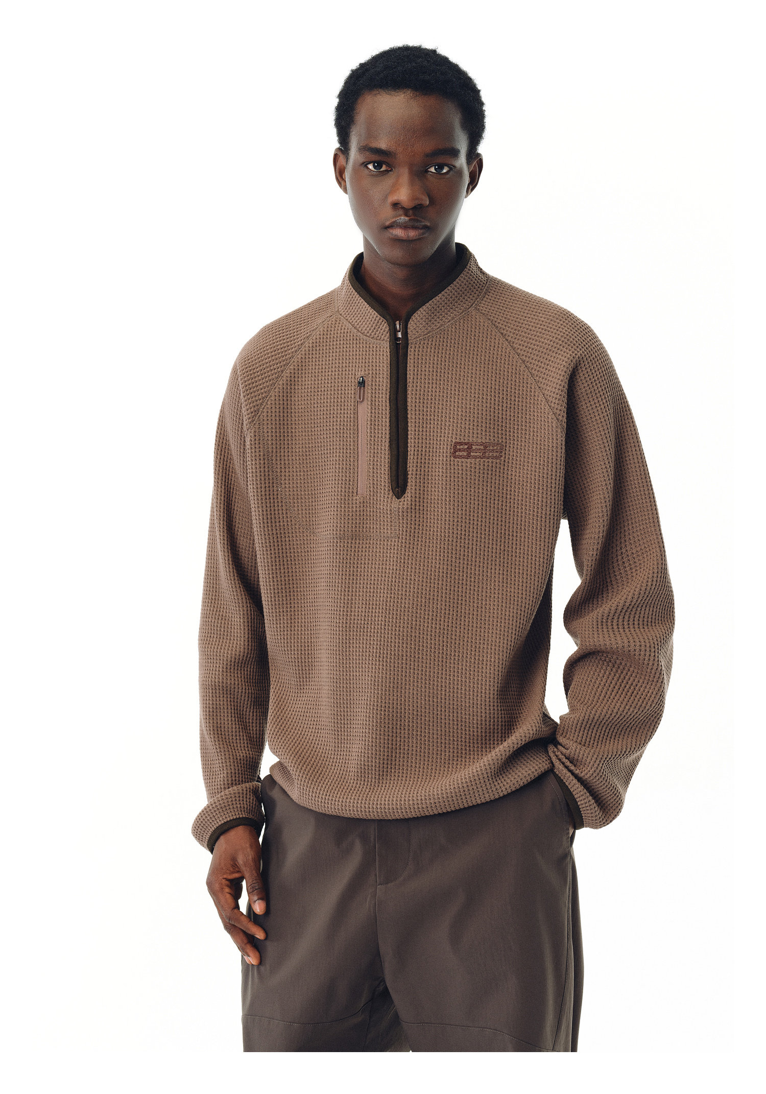 A person stands against a white background wearing the EastLyst Heavyweight Magnetic Waffle Knit Pullover Hoodie with matching brown pants, looking directly at the camera with a neutral expression.