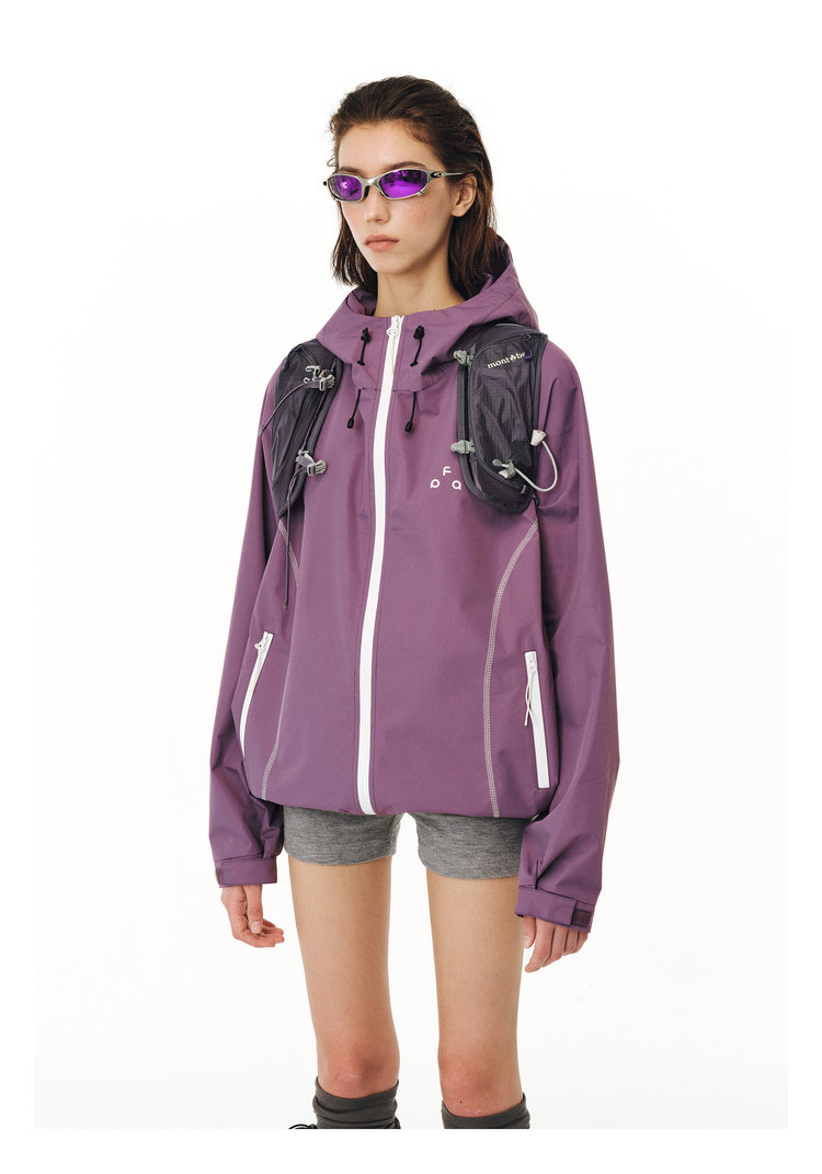 A person models an EastLyst protective outdoor jacket in purple, paired with gray shorts, black knee-high socks, gear harness, and reflective purple sunglasses against a plain white background.