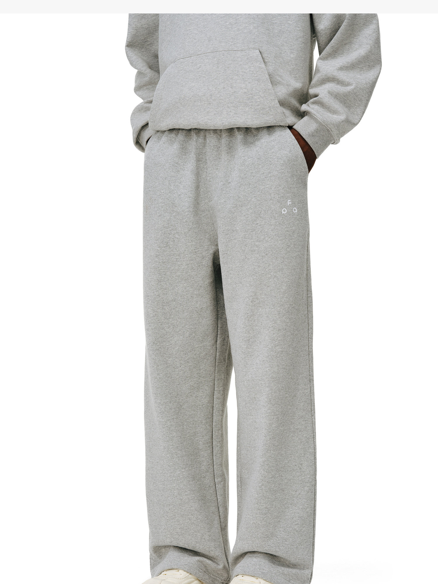 The image shows only the lower torso and legs of a person wearing EastLyst Heavyweight French Terry Sweatpants in light grey, standing against a plain white background with hands tucked into a matching sweatshirt's pocket.
