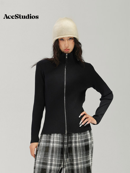 Model wearing a black ribbed zip-up sweater with a black-and-white plaid skirt and knit beanie.