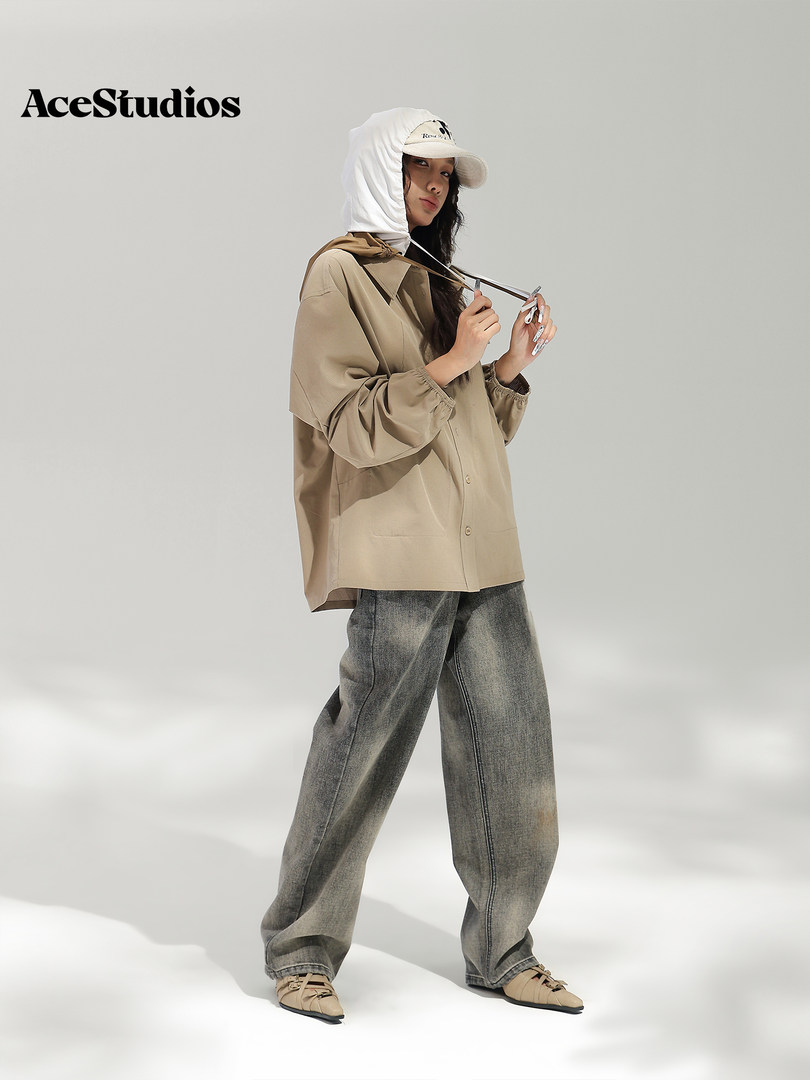 Model wearing a beige oversized jacket, white cap, and loose gray jeans.