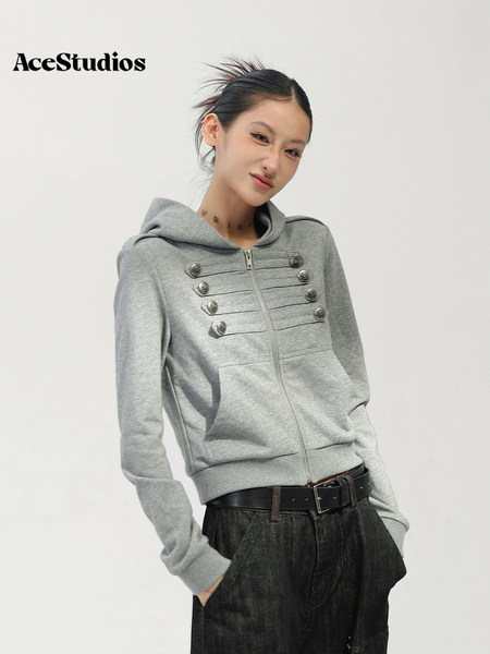 Model wearing a gray zip-up hooded jacket with decorative buttons and black textured trousers.