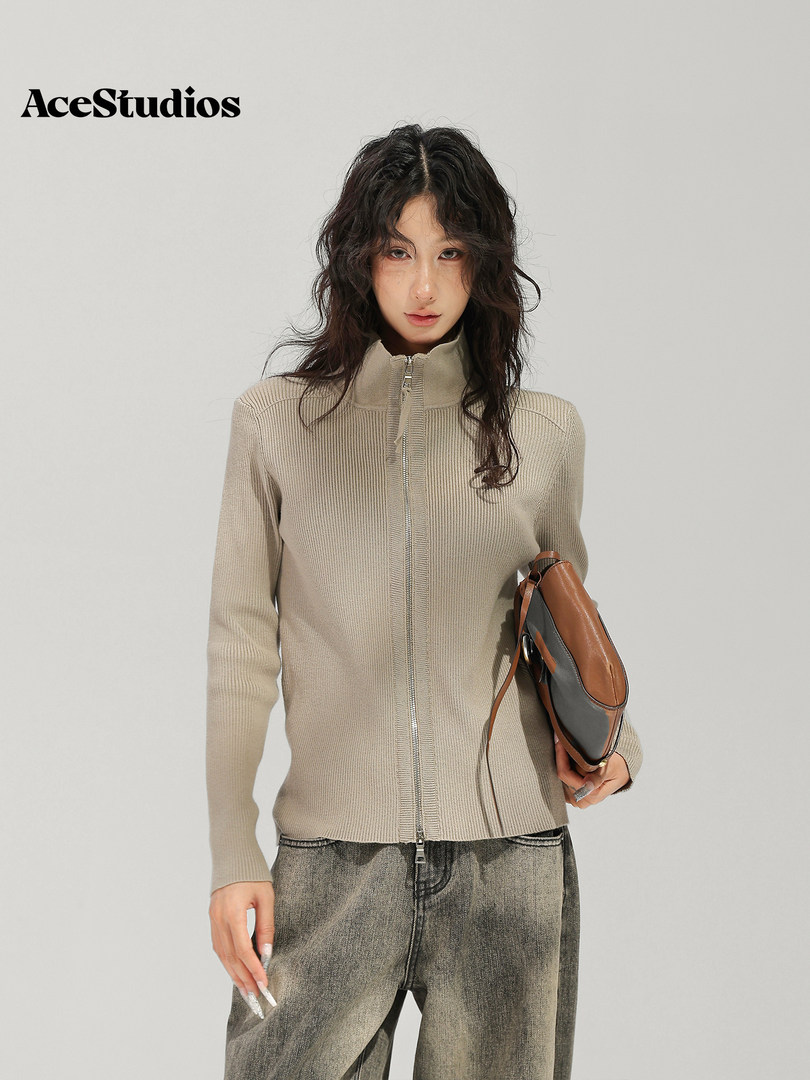 Model wearing a beige ribbed knit cardigan with textured gray jeans and carrying a shoulder bag.