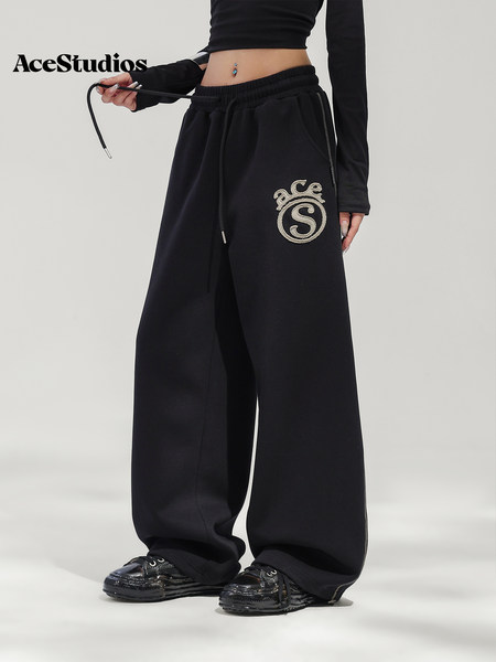 Model wearing black wide-leg sweatpants with an embroidered crest logo.