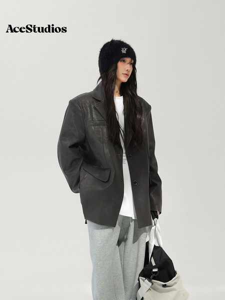 Model wearing a black leather blazer with gray sweatpants, a furry hat, and a shoulder bag.