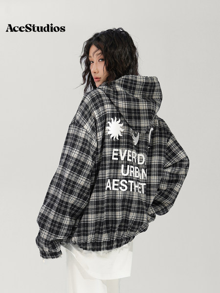 Model wearing a black-and-white plaid hooded streetwear jacket with graphic lettering on the back