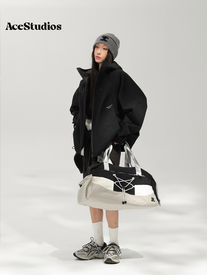 Model wearing a black oversized jacket and beanie with a large black-and-white duffel bag and sneakers.